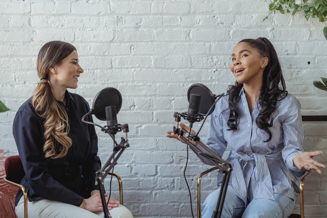 duas mulheres conversando em na frente de microfones, em um programa de podcast